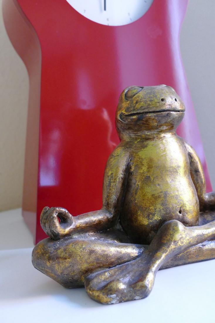 Frosch-Figur in Yoga-Haltung vor rotem Hintergrund